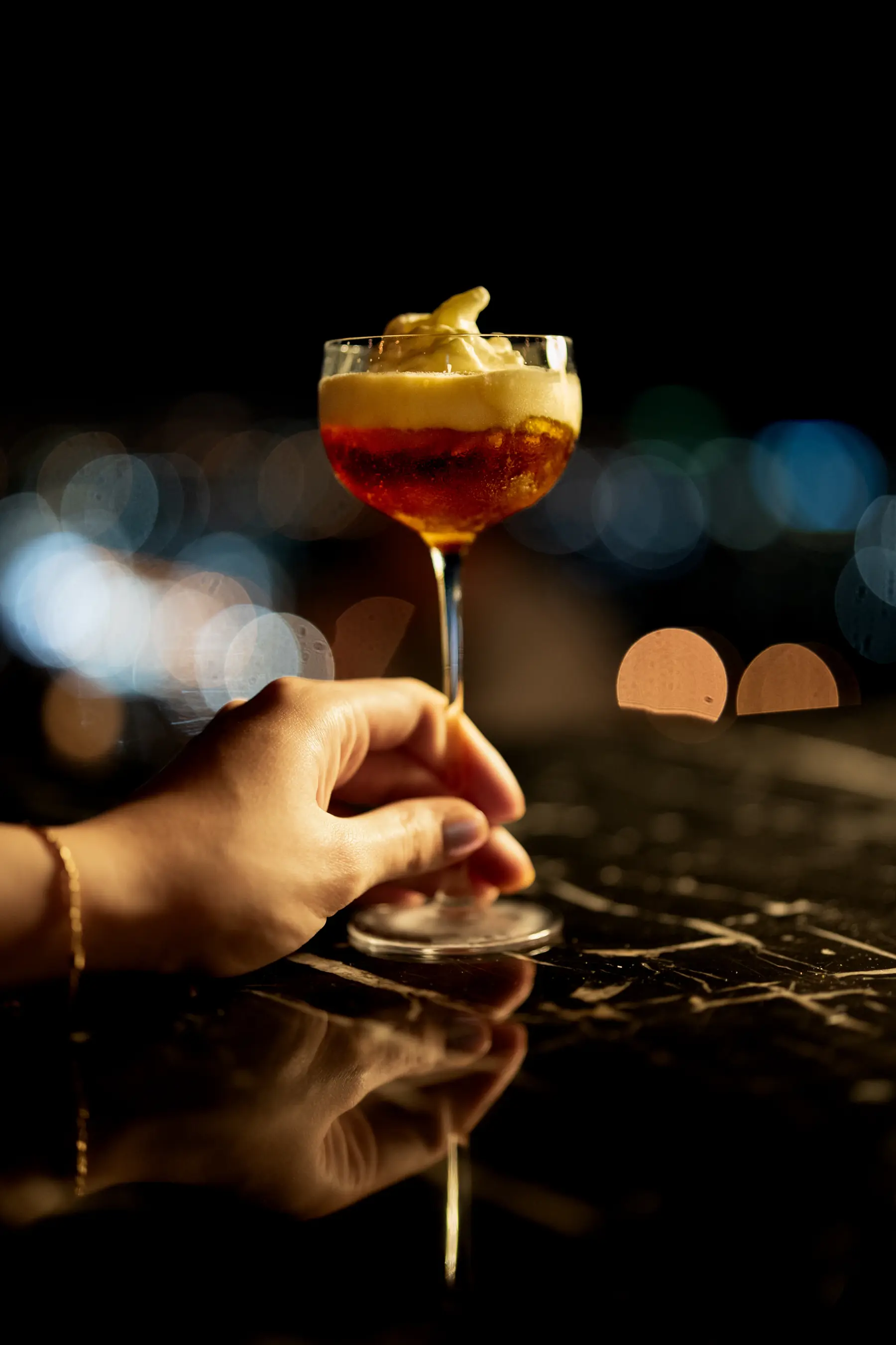 A hand holding an amber cocktail against softly blurred evening lights