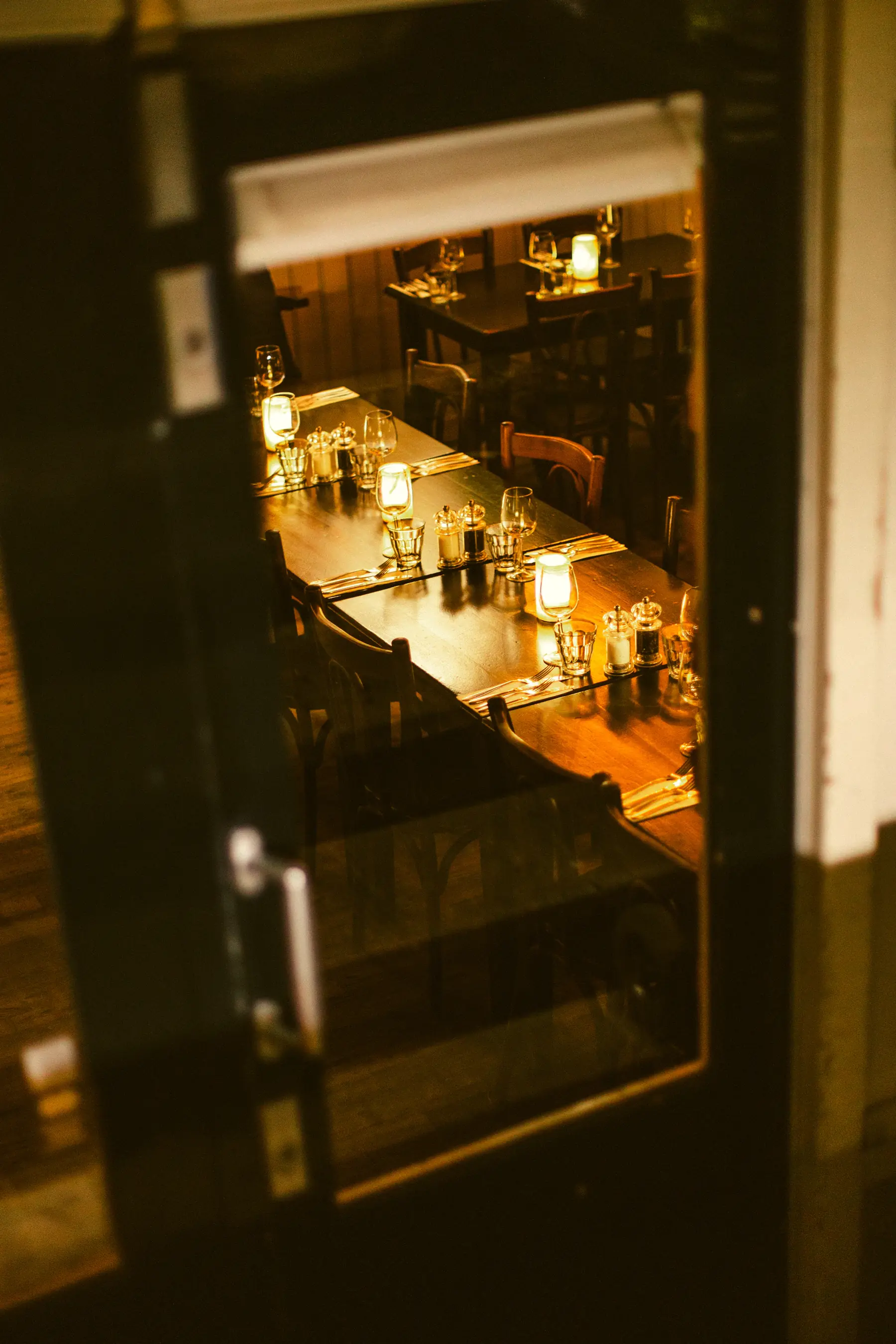 Warm candlelit restaurant tables seen through soft window reflections