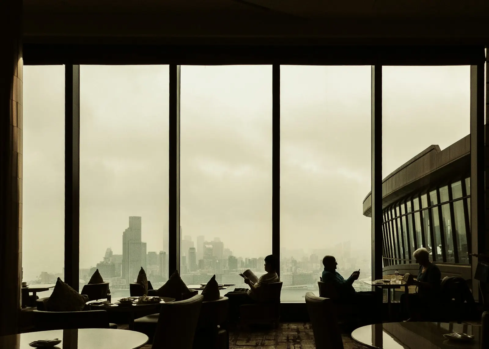 Hotel guests relaxing by panoramic windows over a misty Hong Kong skyline
