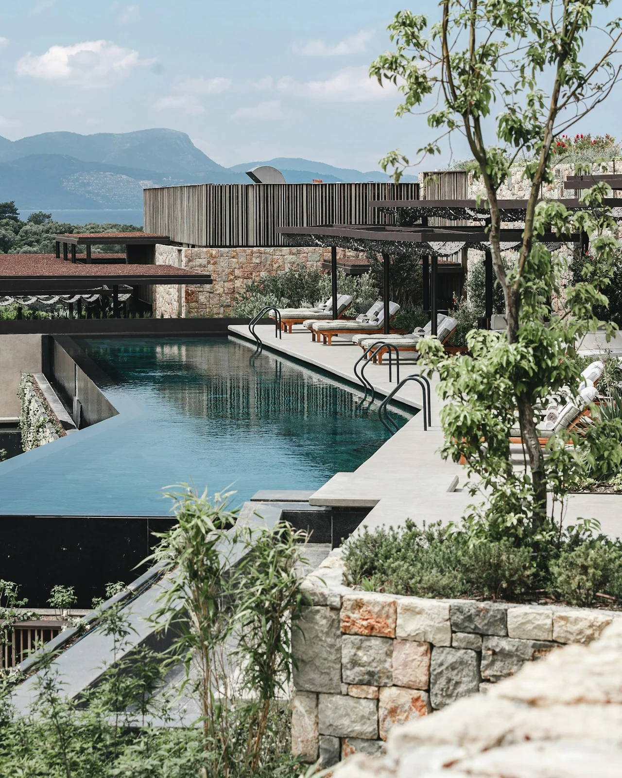 A contemporary resort with an infinity pool, stone terraces and a mountain backdrop